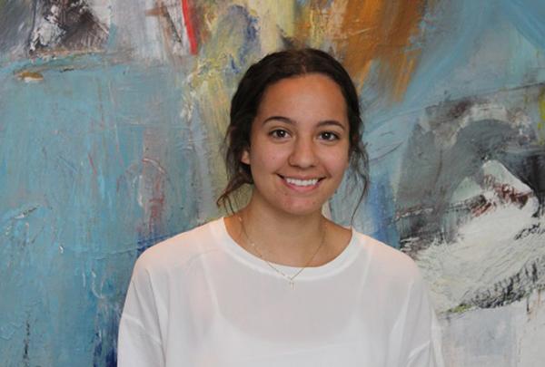 澳门足彩app intern Camila Moreno smiling in front of colorful artwork.
